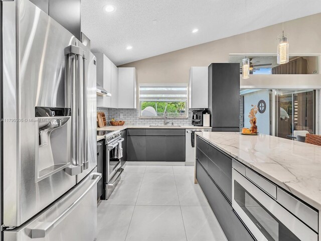 kitchen featuring light stone counters, a sink, a textured ceiling, decorative backsplash, and appliances with stainless steel finishes