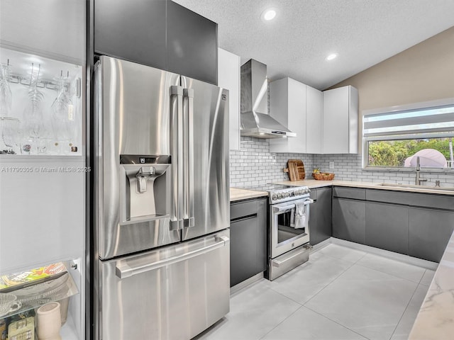 kitchen featuring stainless steel appliances, a sink, wall chimney exhaust hood, decorative backsplash, and a textured ceiling