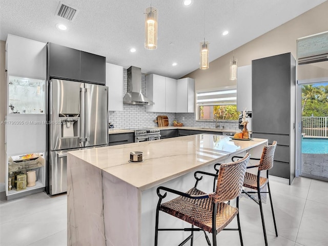 kitchen with wall chimney exhaust hood, stainless steel appliances, a healthy amount of sunlight, backsplash, and a kitchen island