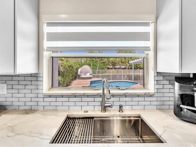 kitchen with light stone countertops, a sink, backsplash, and white cabinetry