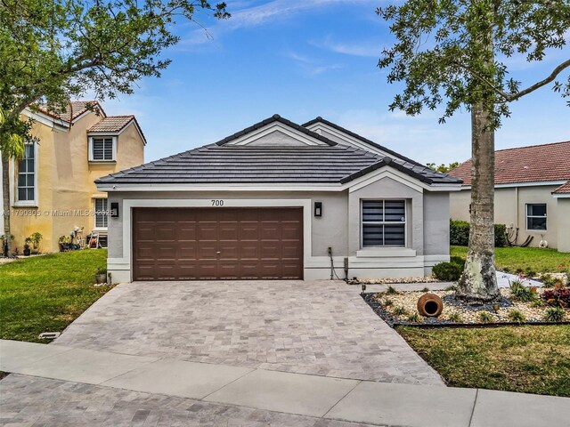 ranch-style house with a tile roof, a garage, driveway, a front yard, and stucco siding