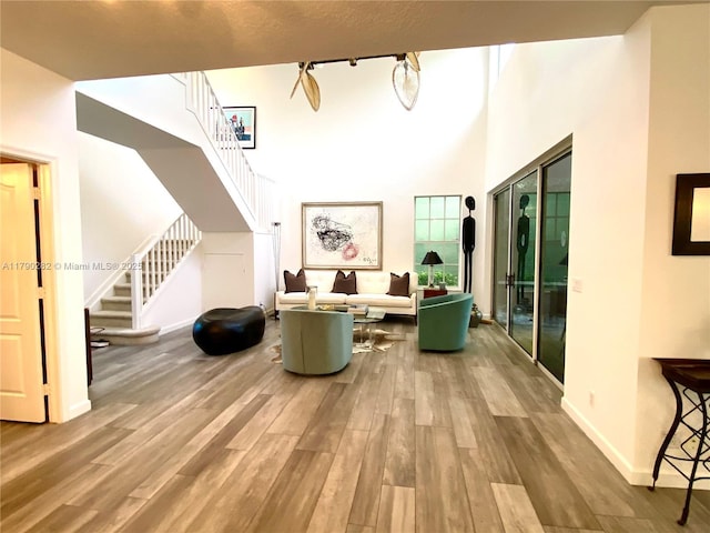 living room featuring a high ceiling, baseboards, wood finished floors, and stairs