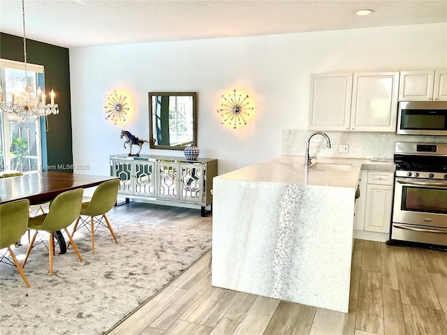 kitchen featuring a sink, light wood finished floors, an inviting chandelier, and stainless steel appliances