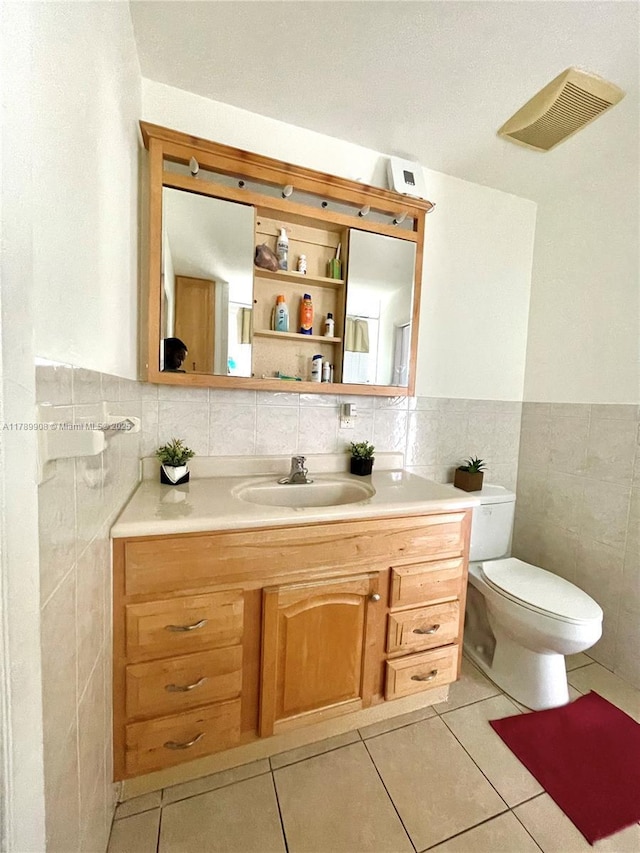 half bathroom with tile walls, vanity, toilet, visible vents, and tile patterned flooring