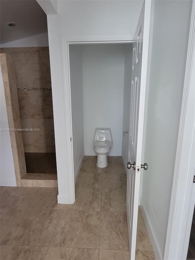 bathroom featuring toilet, a tile shower, and tile patterned flooring
