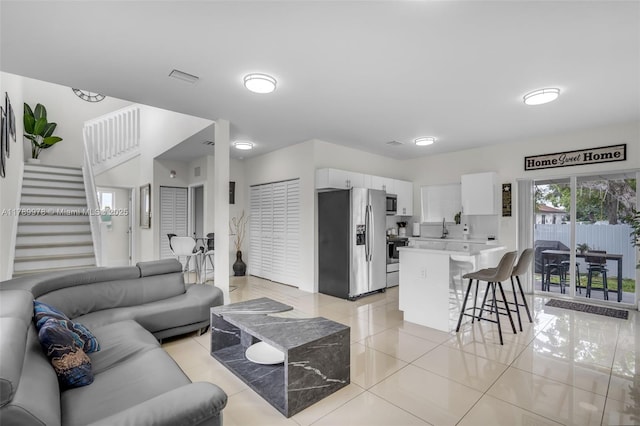 living area with light tile patterned flooring, visible vents, and stairs