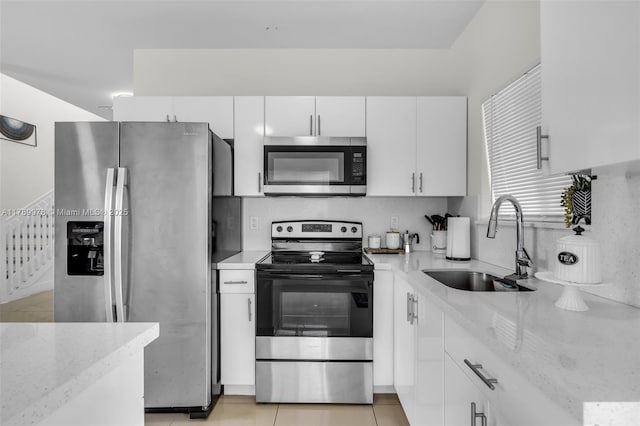 kitchen with a sink, white cabinets, light stone counters, and stainless steel appliances