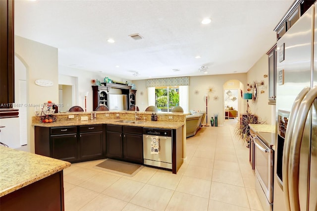 kitchen featuring light stone counters, stainless steel appliances, a sink, arched walkways, and open floor plan