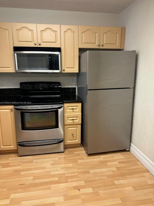 kitchen featuring baseboards, dark countertops, stainless steel appliances, and light wood-type flooring