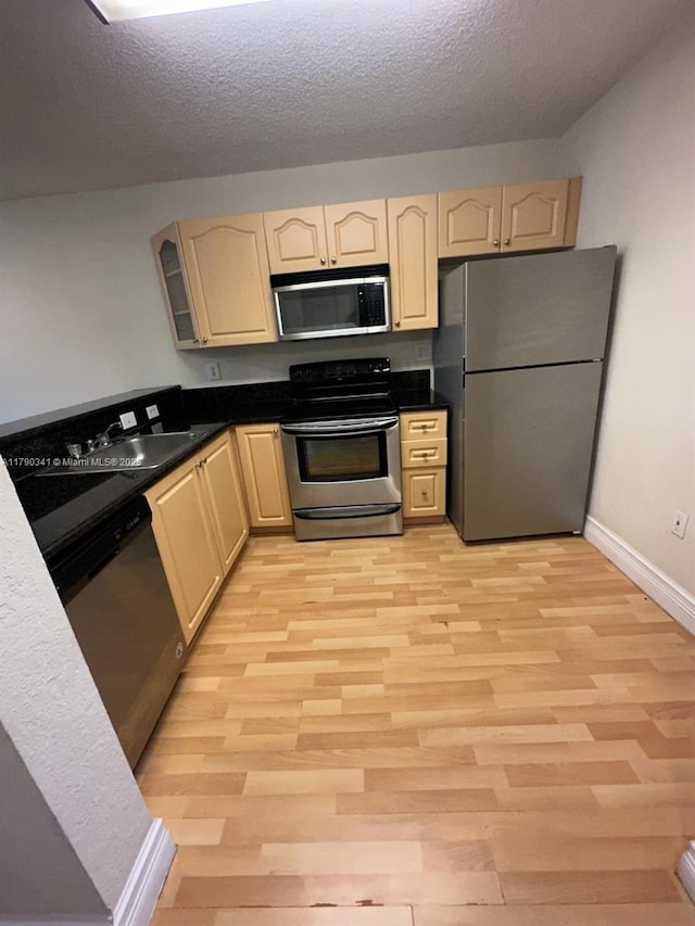 kitchen featuring light wood finished floors, stainless steel appliances, a sink, a textured ceiling, and baseboards
