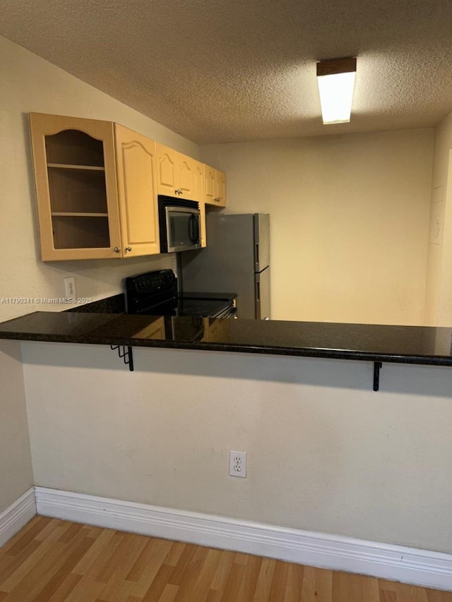 kitchen featuring wood finished floors, range with electric cooktop, stainless steel microwave, a peninsula, and freestanding refrigerator