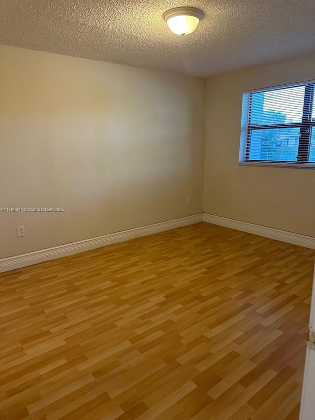 empty room featuring baseboards, a textured ceiling, and light wood-style flooring