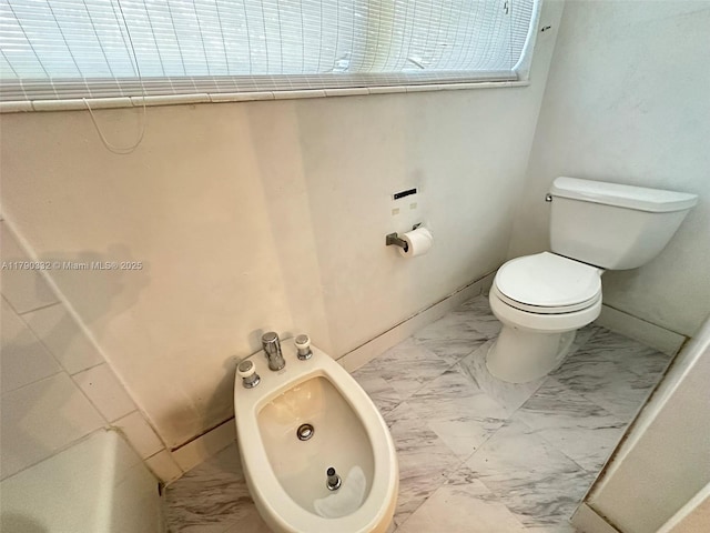 bathroom featuring toilet, a bidet, marble finish floor, and baseboards