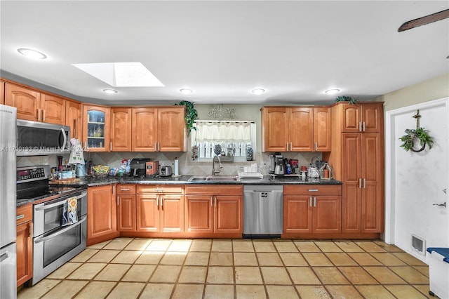 kitchen featuring brown cabinets, appliances with stainless steel finishes, a sink, tasteful backsplash, and a skylight