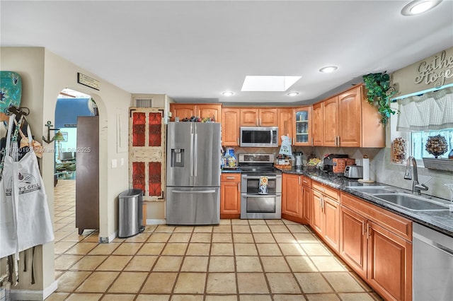 kitchen featuring dark countertops, appliances with stainless steel finishes, a sink, tasteful backsplash, and a skylight