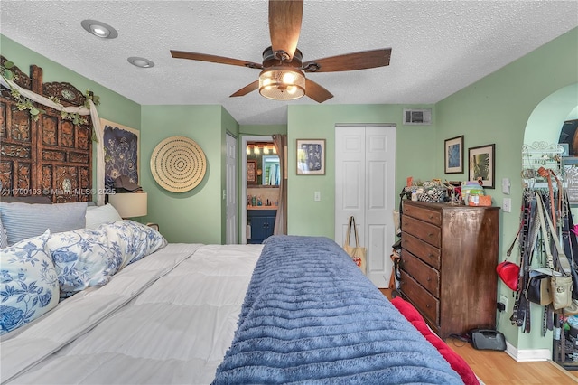 bedroom with arched walkways, a textured ceiling, visible vents, and wood finished floors