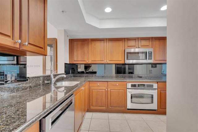 kitchen featuring dark stone counters, a sink, brown cabinets, light tile patterned floors, and stainless steel appliances