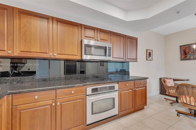 kitchen with white oven, brown cabinets, light tile patterned floors, black electric stovetop, and stainless steel microwave