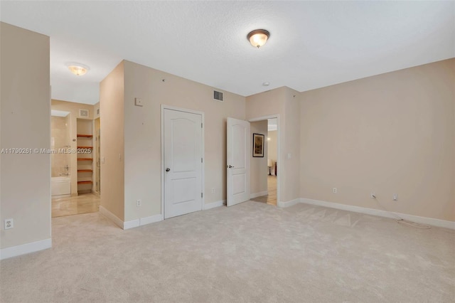 unfurnished bedroom featuring visible vents, baseboards, a textured ceiling, light colored carpet, and ensuite bathroom
