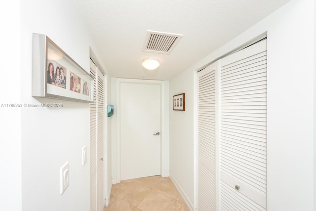 corridor featuring a textured ceiling, visible vents, and baseboards