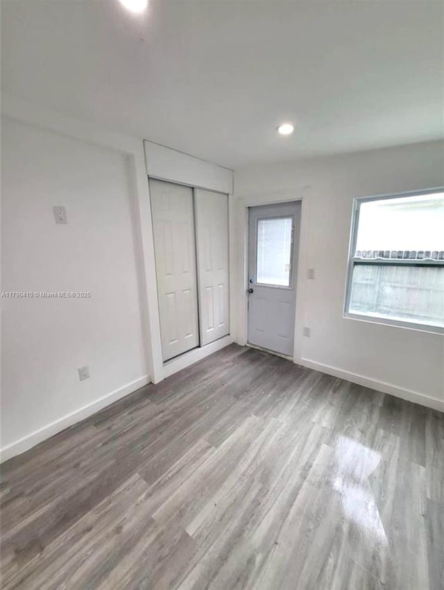 unfurnished bedroom featuring baseboards, a closet, recessed lighting, and wood finished floors