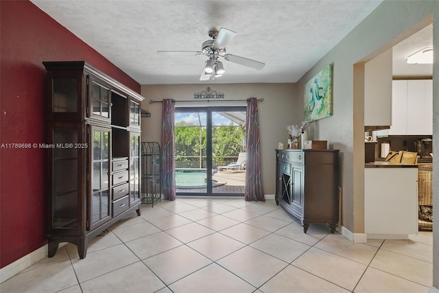 doorway with baseboards, a ceiling fan, and light tile patterned floors