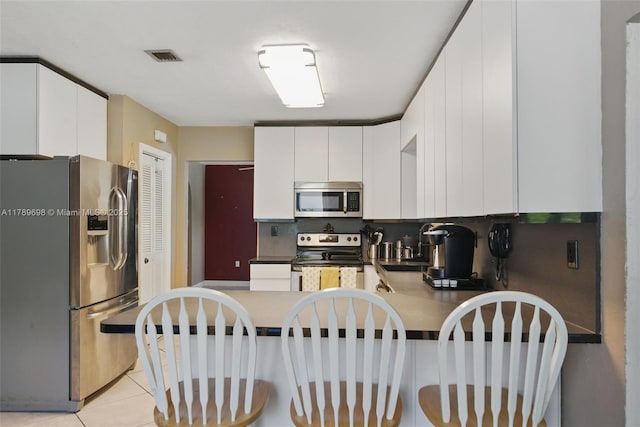 kitchen featuring a peninsula, white cabinetry, stainless steel appliances, and visible vents