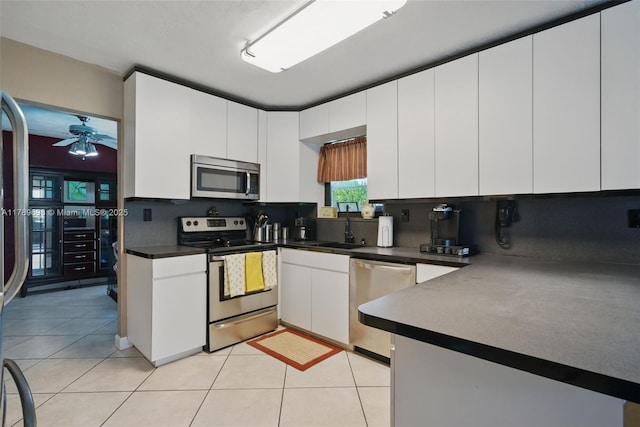 kitchen with white cabinets, stainless steel appliances, dark countertops, light tile patterned flooring, and ceiling fan