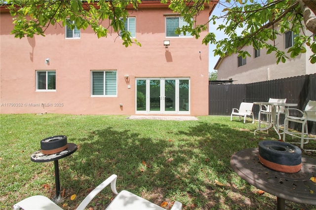 rear view of house with stucco siding, fence, and a lawn