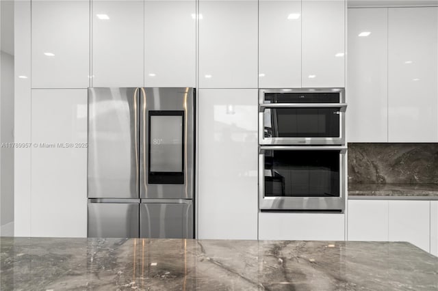 kitchen with white cabinets, dark stone countertops, appliances with stainless steel finishes, and modern cabinets