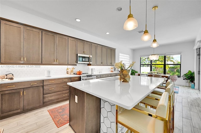8650 NW 39th Ct, Coral Springs, FL 33065 - kitchen featuring light wood-style flooring, appliances with stainless steel finishes, a kitchen island, and decorative light fixtures