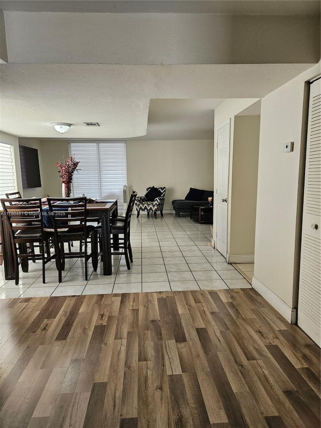 dining space featuring light wood-style flooring, a textured ceiling, and baseboards