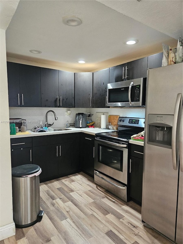 kitchen with appliances with stainless steel finishes, a sink, light wood-style floors, and dark cabinetry