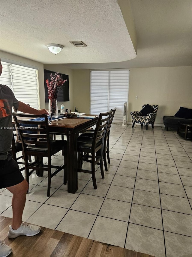 dining space featuring baseboards, visible vents, a textured ceiling, and light tile patterned floors