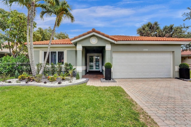 mediterranean / spanish-style house with stucco siding, an attached garage, french doors, decorative driveway, and a front yard