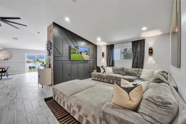 living area featuring light wood finished floors, vaulted ceiling, baseboards, visible vents, and a ceiling fan