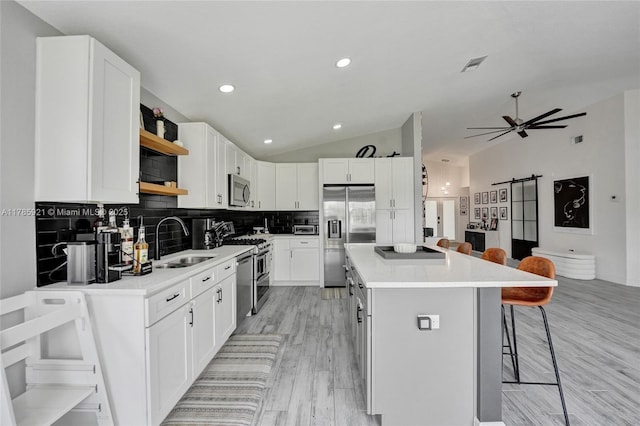 kitchen with a sink, vaulted ceiling, a kitchen bar, open shelves, and appliances with stainless steel finishes