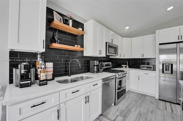kitchen featuring stainless steel appliances, open shelves, backsplash, a sink, and white cabinetry