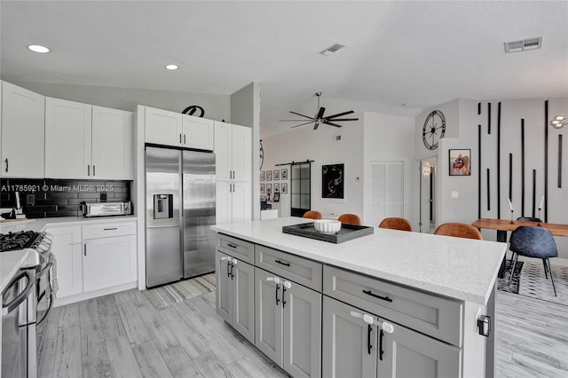 kitchen featuring a center island, a ceiling fan, lofted ceiling, appliances with stainless steel finishes, and visible vents