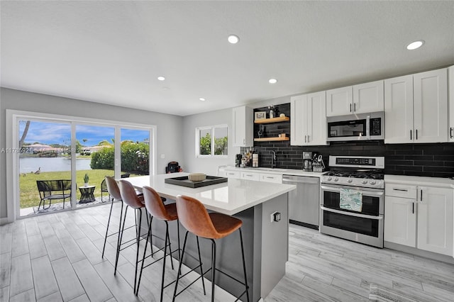 kitchen featuring light countertops, open shelves, a breakfast bar, a kitchen island, and appliances with stainless steel finishes