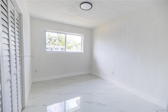 spare room featuring a textured ceiling, marble finish floor, and baseboards
