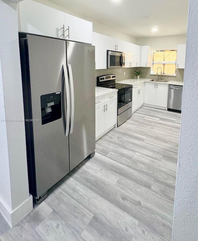 kitchen with a sink, decorative backsplash, stainless steel appliances, light countertops, and white cabinets