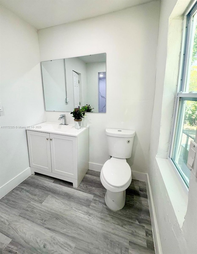 half bathroom featuring plenty of natural light, baseboards, vanity, and toilet