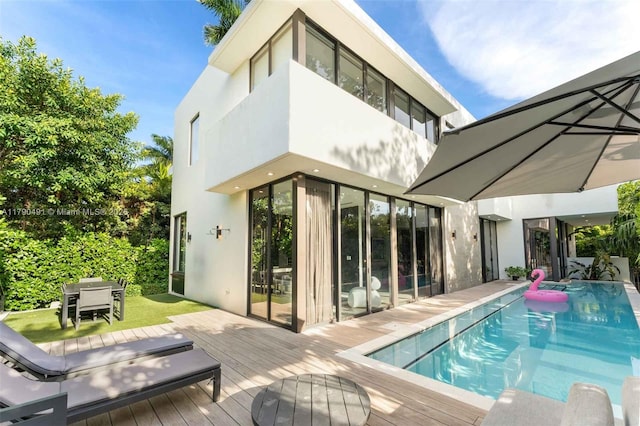 back of property featuring a deck, an outdoor pool, and stucco siding