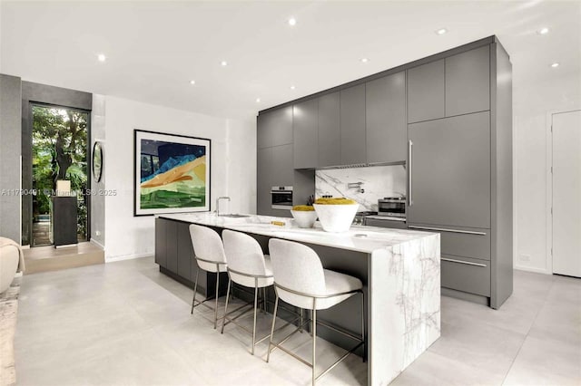 kitchen featuring gray cabinetry, modern cabinets, a large island with sink, and oven