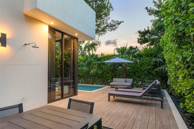 deck at dusk with outdoor dining area and an outdoor pool