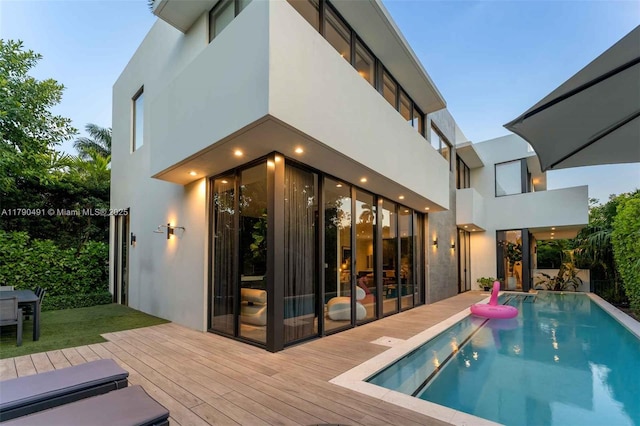 back of house with stucco siding, an outdoor pool, and a wooden deck