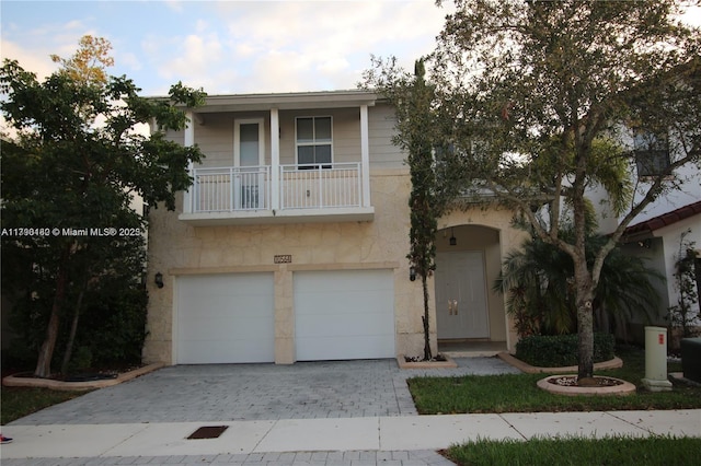 view of front of home featuring an attached garage, decorative driveway, stone siding, and a balcony
