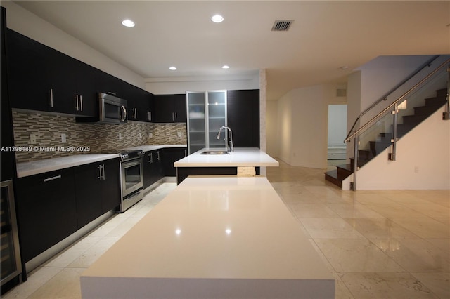 kitchen with a sink, dark cabinetry, light countertops, appliances with stainless steel finishes, and visible vents