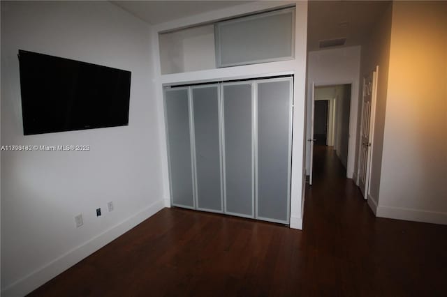 unfurnished bedroom featuring baseboards, wood finished floors, visible vents, and a closet